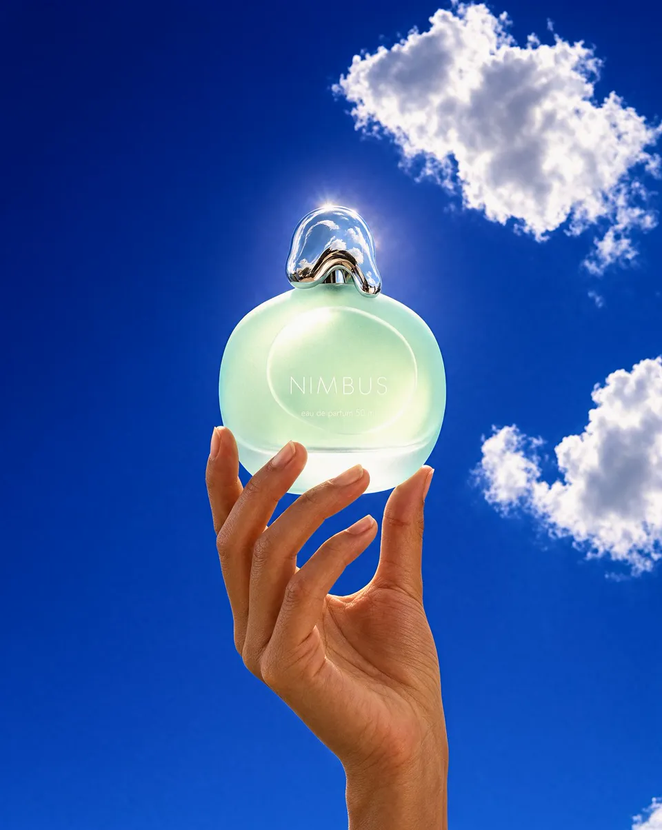 Fragrance campaign image of a frosted perfume bottle held against a blue sky